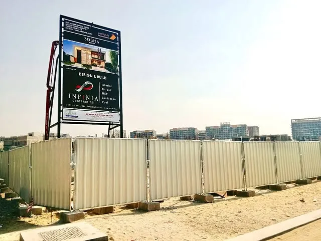 A large white fence is under construction, surrounding a busy construction site in the background.
